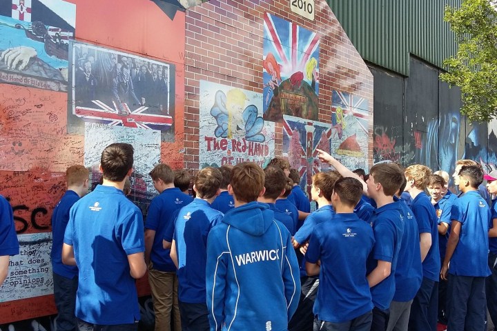 a group of school kids studying the murals on the peace wall